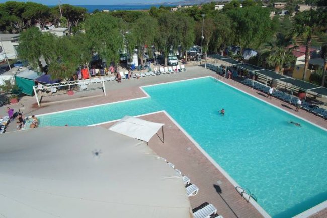 Vista dall'alto di una piscina all'aperto con lettini bianchi e alberi circostanti.