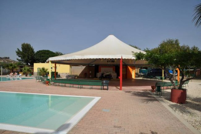 Piscina con tettoia a tenda bianca e area relax con sedie, in un ambiente all'aperto.