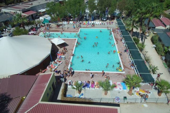 Veduta dall'alto di una piscina esterna affollata con lettini e palme intorno.