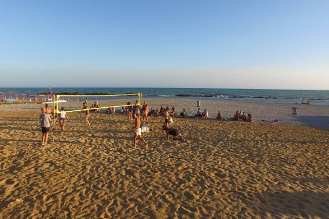 Persone giocano a pallavolo sulla spiaggia al tramonto, con il mare sullo sfondo.