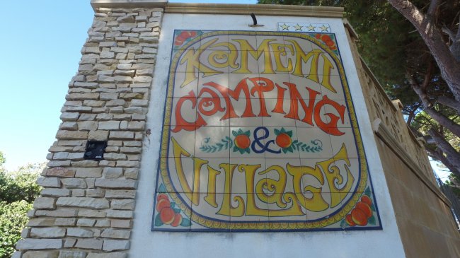 Insegna colorata di un camping e village, su un muro in pietra.