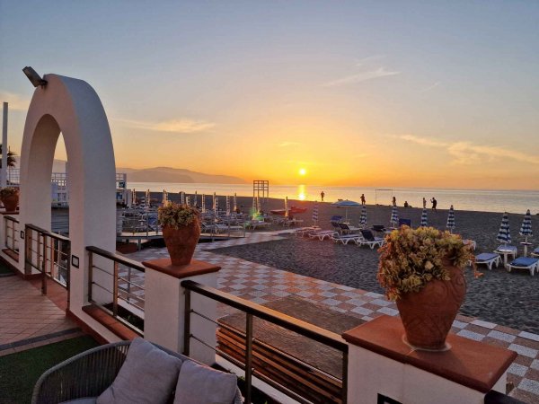 Tramonto sulla spiaggia con lettini e fiori in vasi.