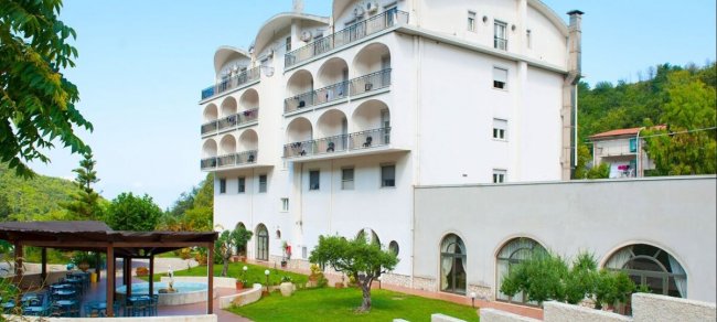 Un edificio bianco con balconi e un giardino curato con alberi e un patio.