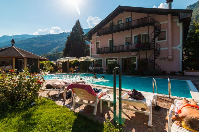 Piscina vicino a un edificio in montagna, persone su lettini.
