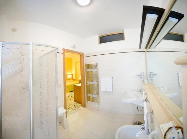 Bagno moderno con doccia, specchio lungo e arredi bianchi.