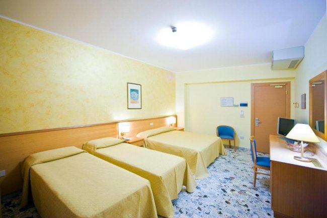 Una camera d'albergo con tre letti singoli coperti da coperte beige.