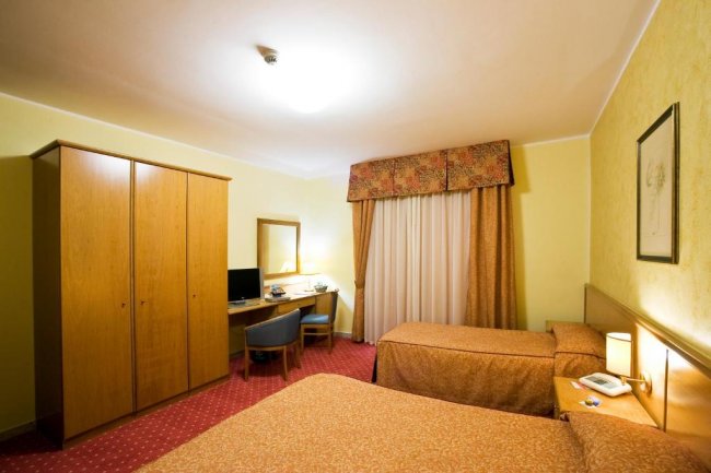 Camera d'albergo con due letti singoli, armadio, scrivania e sedia.