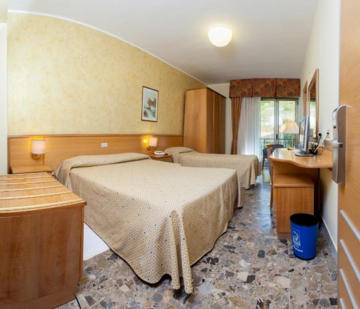 Camera d'albergo con due letti singoli, pavimento in marmo e mobili in legno chiaro.