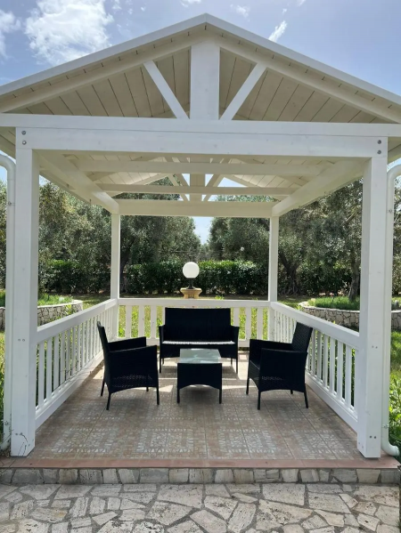 Un gazebo bianco con mobili neri in un giardino verde.