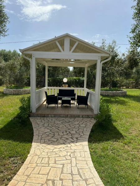Gazebo bianco con mobili neri, situato su un prato verde con sentiero di pietra.