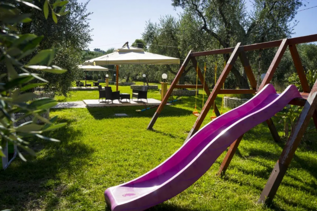 Scivolo rosa in un parco giochi con sedie e ombrelloni.
