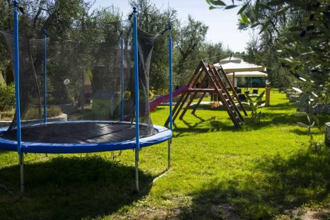 Giardino con trampolino blu, scivolo viola e altalena tra gli alberi.