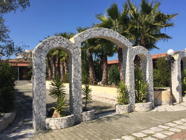 Archi di pietra, piante e palme sotto un cielo limpido.