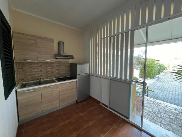 Cucina compatta con armadietti chiari e frigorifero.