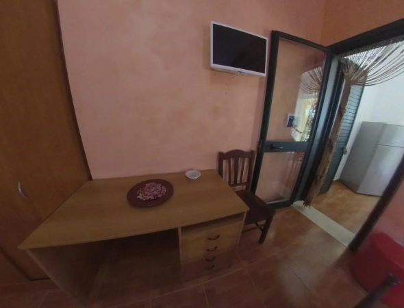 Scrivania di legno con sedia, TV a muro e porta finestra.