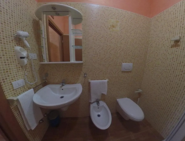 Bagno con lavabo, bidet e wc. Rivestimento mosaico beige e specchio con scaffali.
