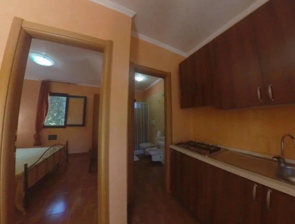 Corridoio con vista su camera da letto e bagno. Cucina con mobili in legno scuro.