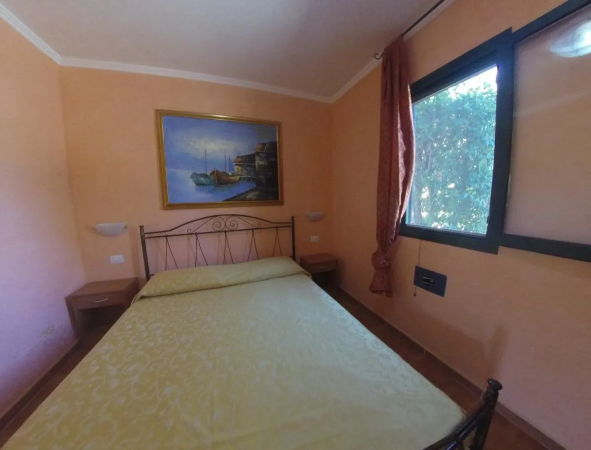 Camera con letto matrimoniale, pareti color pesca, finestra e quadro nautico.