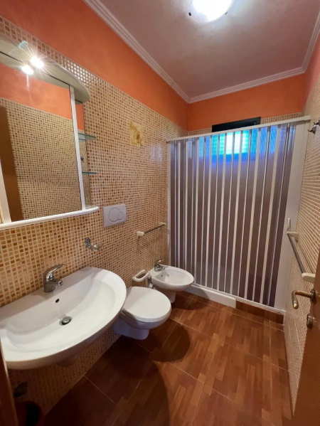 Bagno con doccia, lavabo, WC e bidet, pareti mosaico arancioni.