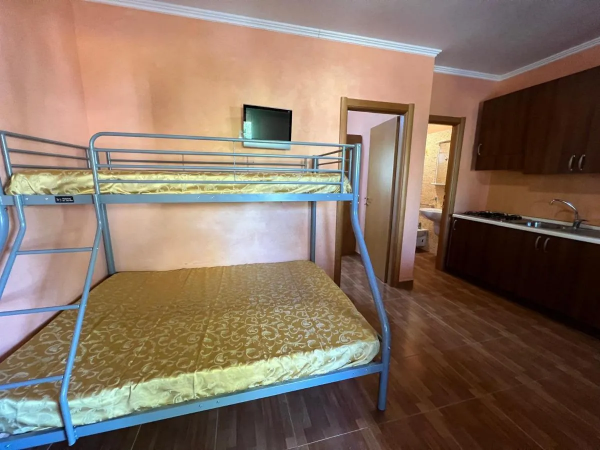 Stanza con letto a castello, piccola TV, cucina in legno.