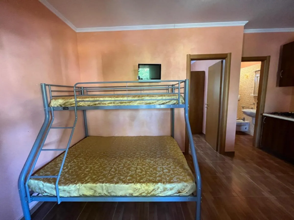 Letto a castello, bagno visibile, cucina in legno sulla destra.