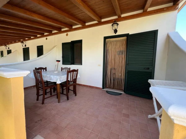 Una veranda con tavolo e sedie in legno, pavimento piastrellato e pareti bianche.