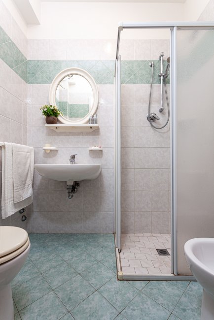 Bagno con doccia, lavabo con specchio rotondo e piastrelle verdi.