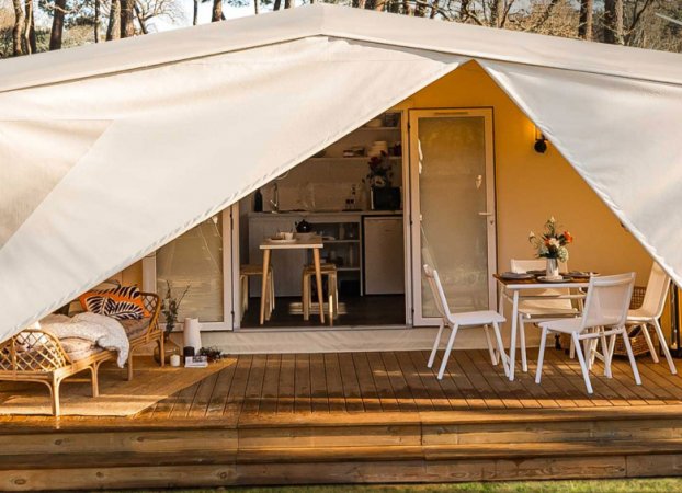 Tenda glamping con veranda, tavolo da pranzo e sedie.