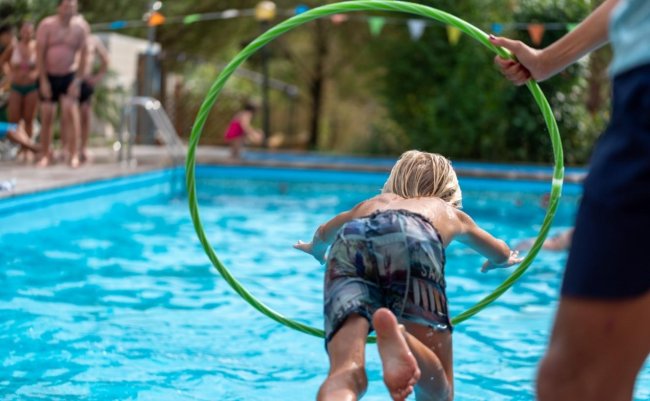 Bambino salta attraverso un cerchio verde verso una piscina.