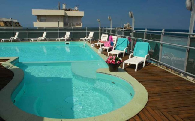 Piscina con solarium, lettini bianchi e asciugamani colorati su una terrazza.
