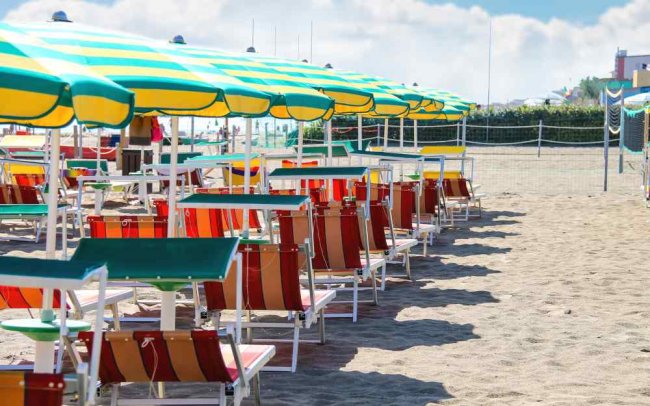 Spiaggia con ombrelloni a righe gialle verdi e lettini colorati in fila.