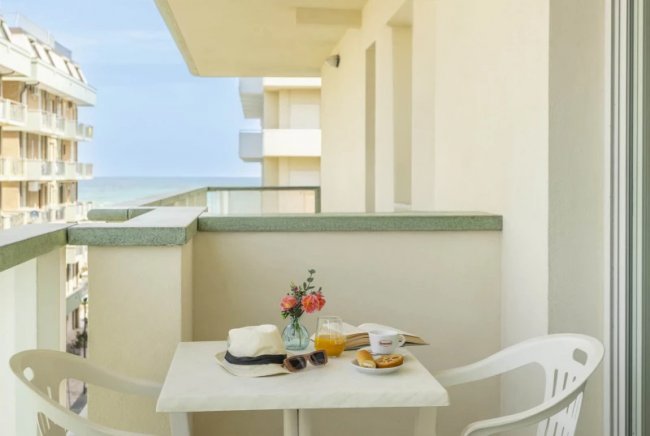 Balcone con tavolo, sedie e colazione al mare.