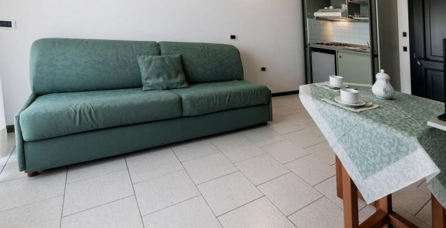 Un soggiorno con divano verde, tavolino apparecchiato e angolo cottura.
