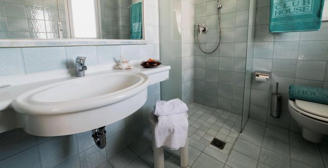 Bagno con lavabo bianco, doccia a vetro e asciugamani appesi.