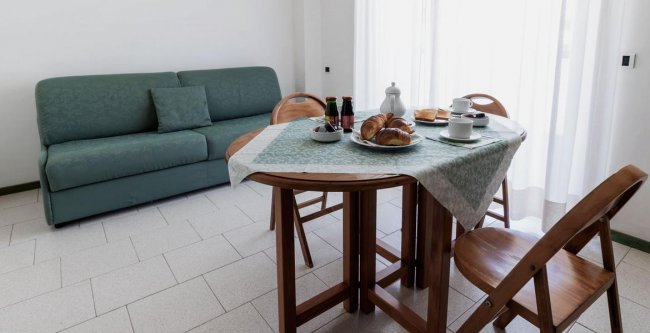 Tavolo da pranzo apparecchiato, divano verde sullo sfondo.