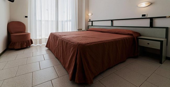 Camera da letto con letto matrimoniale, copriletto marrone e sedia coordinata.