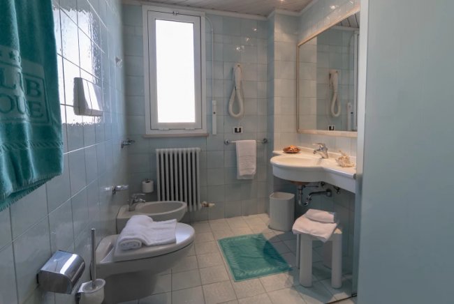 Bagno con lavabo, bidet, finestra e asciugamani bianchi e blu.