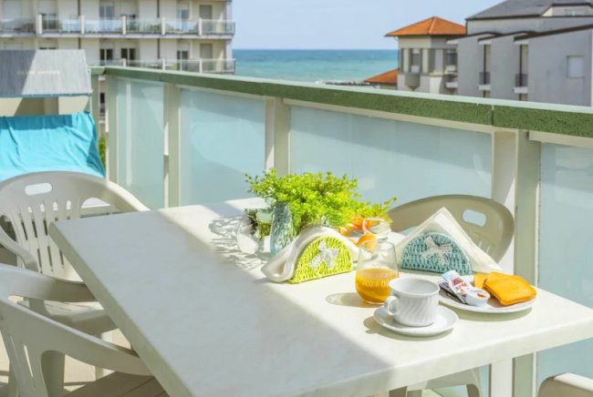 Terrazza con tavolo apparecchiato, sedie bianche e vista mare.