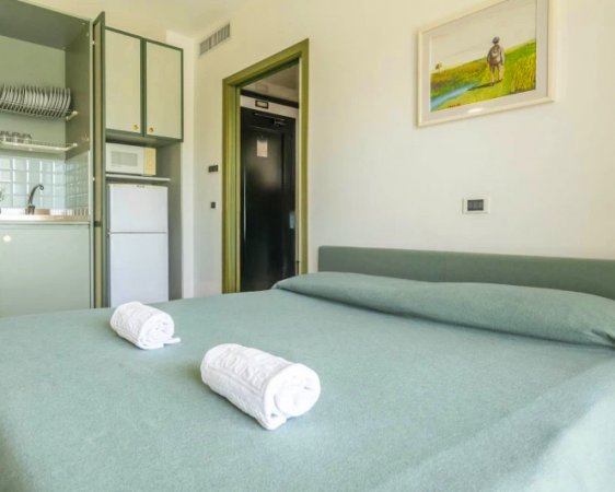 Letto matrimoniale con asciugamani arrotolati, vicino a una cucina.