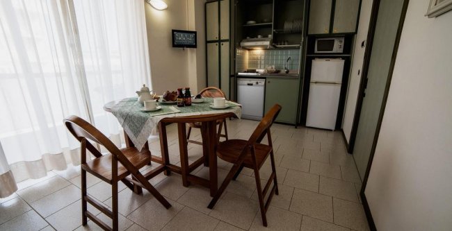 Cucina con tavolo rotondo, sedie di legno e mobili verdi.