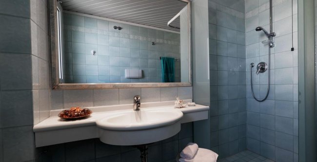 Bagno moderno con lavabo sospeso, specchio ampio e doccia angolare a piastrelle azzurre.