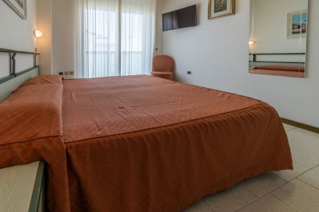 Stanza da letto con letto matrimoniale, TV a parete e sedia accanto a una grande finestra.