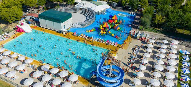 Piscina con scivolo blu e molte sedie a sdraio bianche.