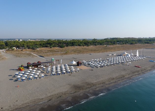 Spiaggia con ombrelloni bianchi e mare a destra.