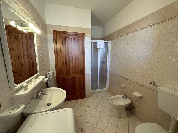 Un bagno con lavandino, doccia, bidet e WC, arredato con mattonelle beige e una porta in legno.