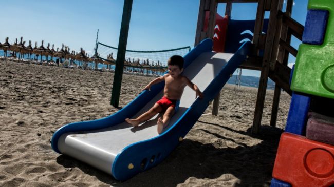 Bambino scende da uno scivolo sulla spiaggia.