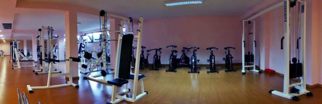 Una palestra con attrezzi e cyclette su pavimento in legno.