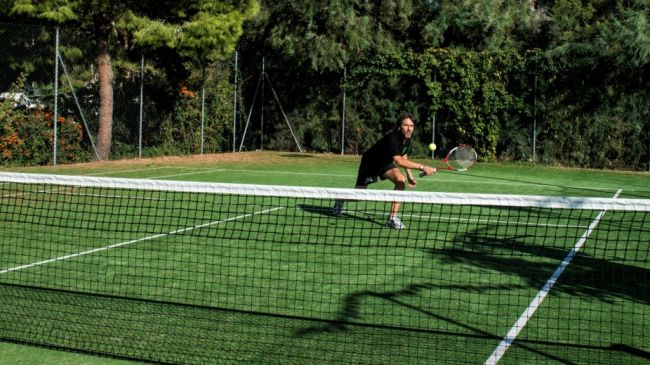 Uomo gioca a tennis su campo in erba.