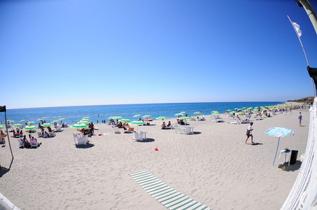 Spiaggia con ombrelloni verdi e cielo azzurro.