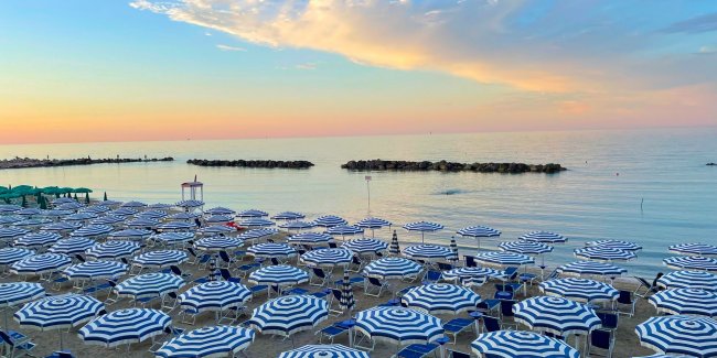 Ombrelloni blu e bianchi al tramonto su una spiaggia.